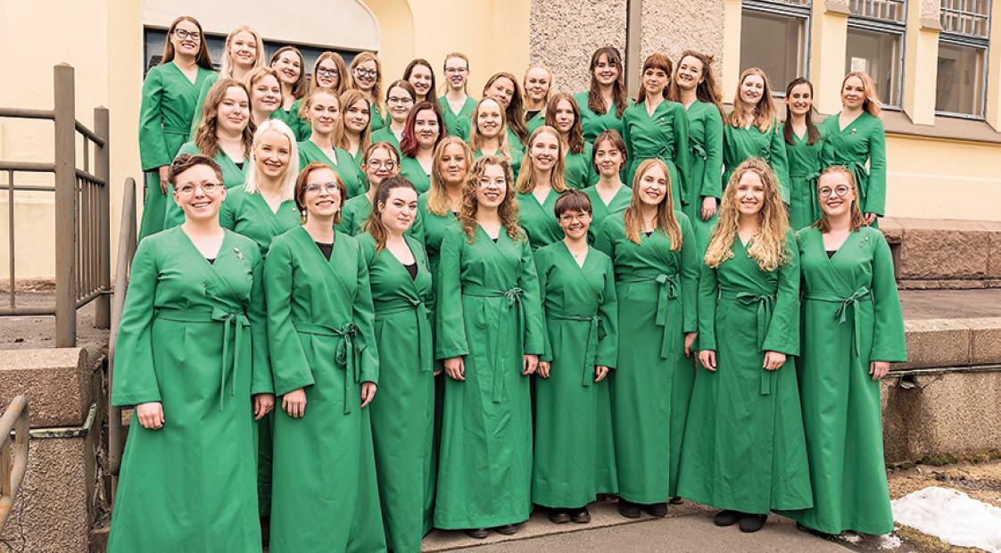 Koristerna står på en trappa klädda i gröna långa klänningar.
